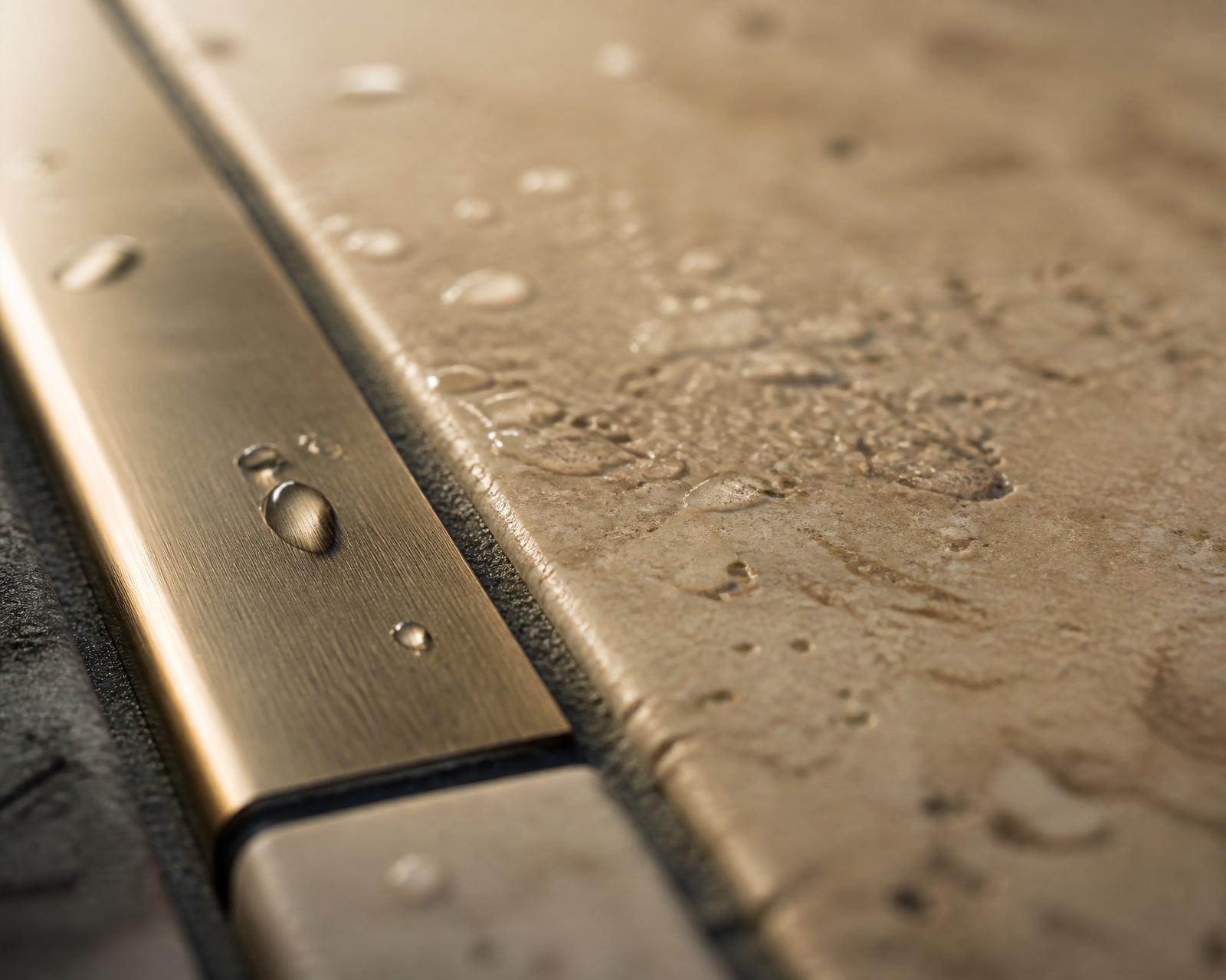 Macro close-up of a honed travertine paver meeting a brushed bronze inlay strip at dawn